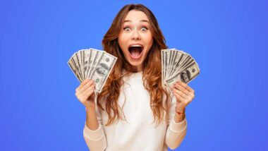 An excited woman holding U.S. cash, representing checks in the mail.