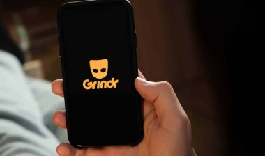 Close up of a man holding a smartphone with the Grindr logo displayed, representing the Grindr lawsuit.