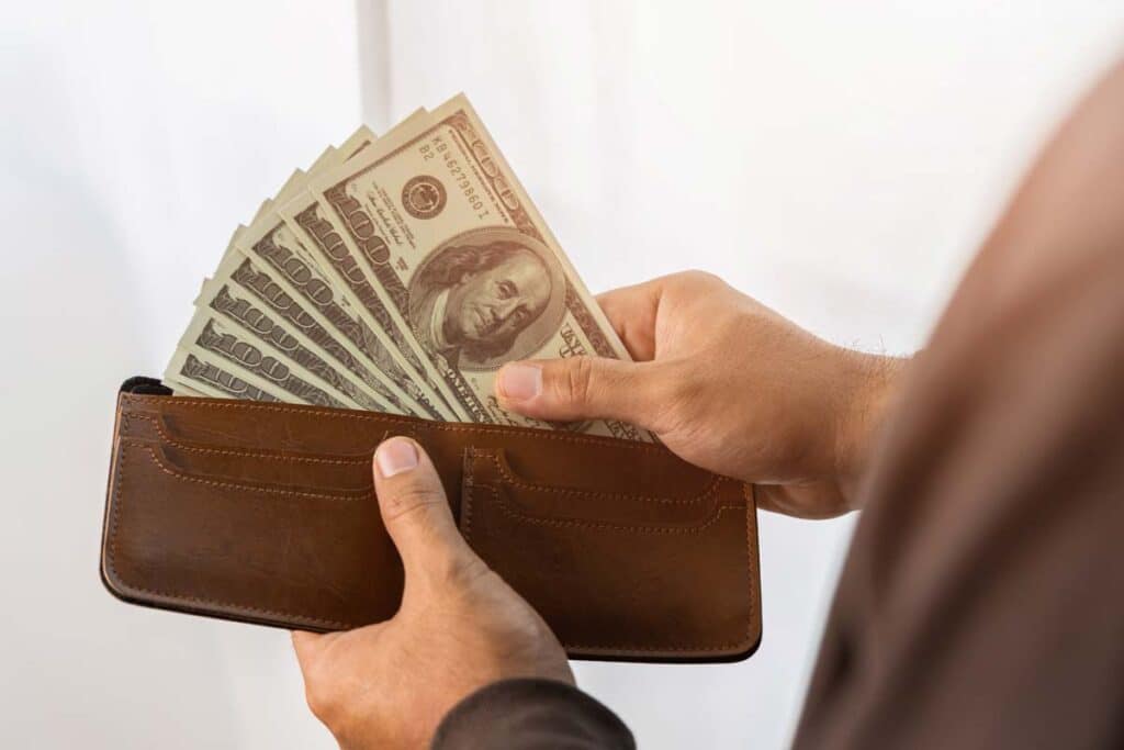 Close up of a man putting cash into his wallet, representing recent class action rebates.