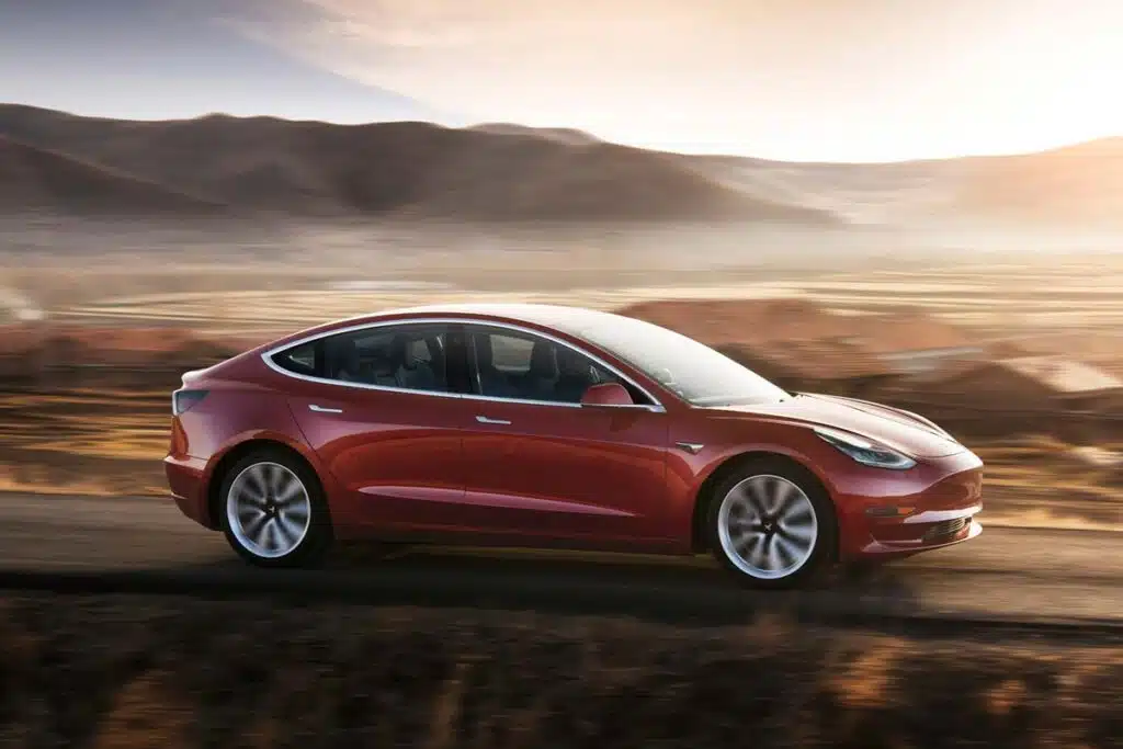 A red Tesla model 3 driving along a roadway, representing the Tesla recall.