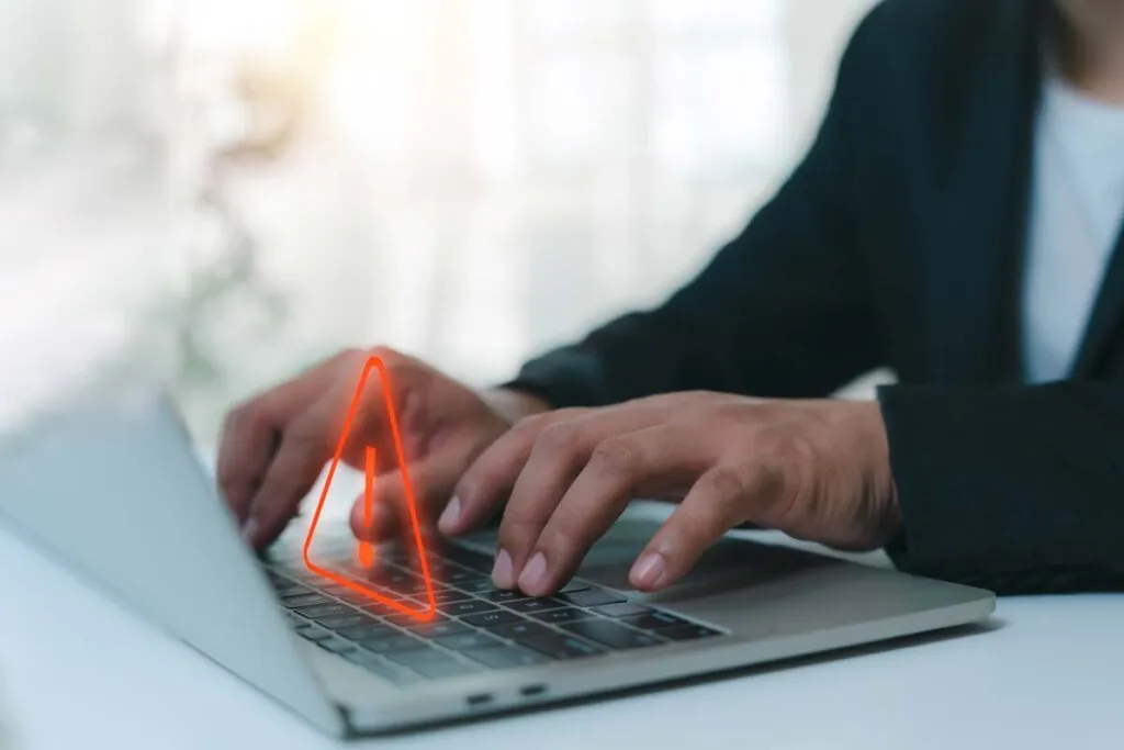 Close up of a woman typing on a laptop with a warning symbol overlay, representing the data collection class actions.