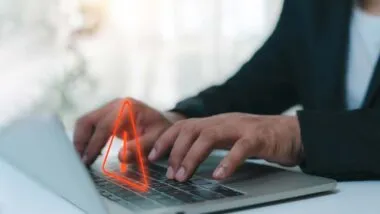 Close up of a woman typing on a laptop with a warning symbol overlay, representing the data collection class actions.