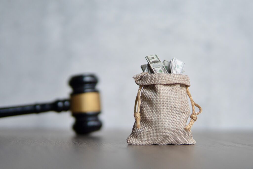 A bag of money next to a Judge's gavel representing company fines.