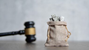 A bag of money next to a Judge's gavel representing company fines.