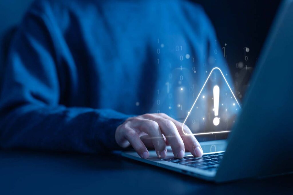 Close up of hands typing on a laptop with a warning sign overlay, representing the data breach class actions.