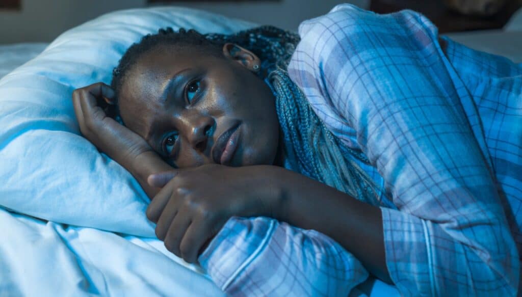 young sad and depressed black African American woman lying on bed at home.