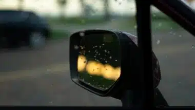 Dewdrops on the side mirror of a car reflecting the sky and trees