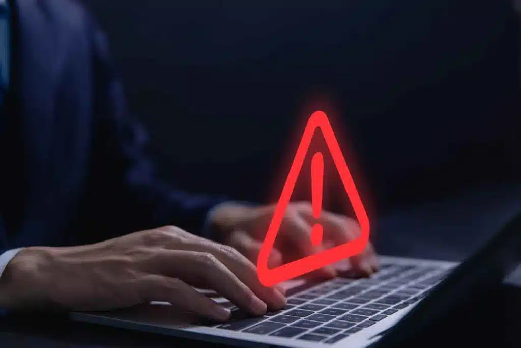 Close up of hands typing on a laptop with a warning symbol overlay, representing the Internet Archive data breach.