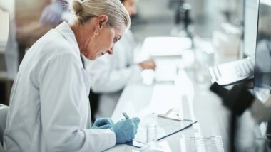 A clinical trial lab worker writing on a clipboard, representing the Cassava settlement.