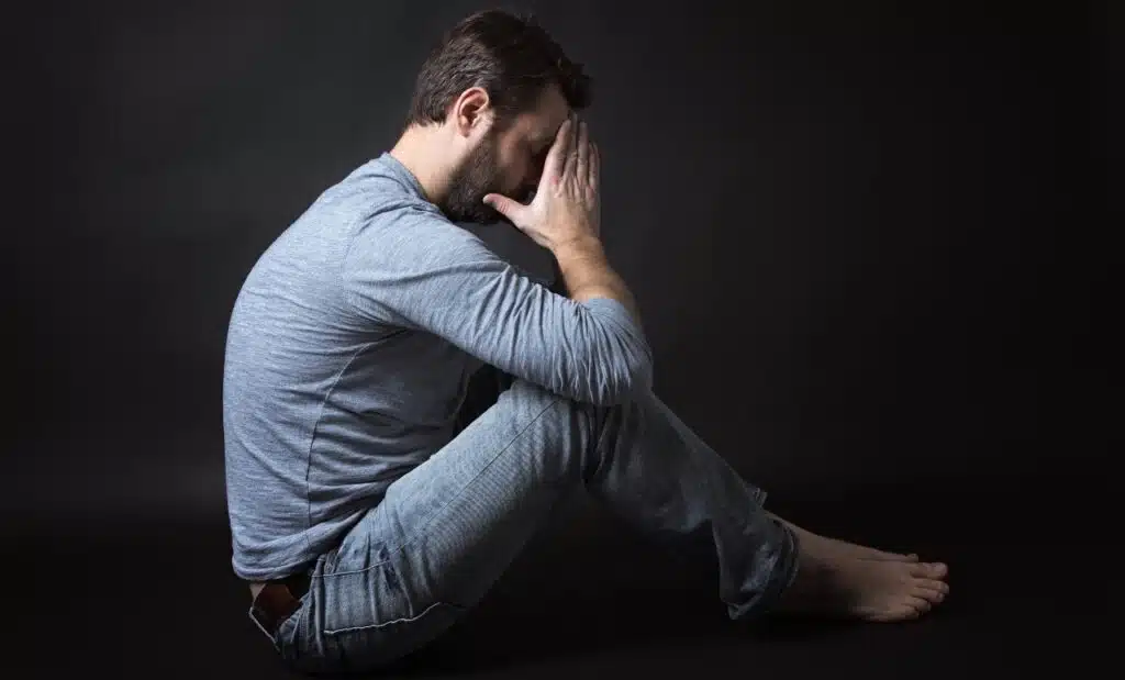 Low key portrait of man sitting in dark and contemplating