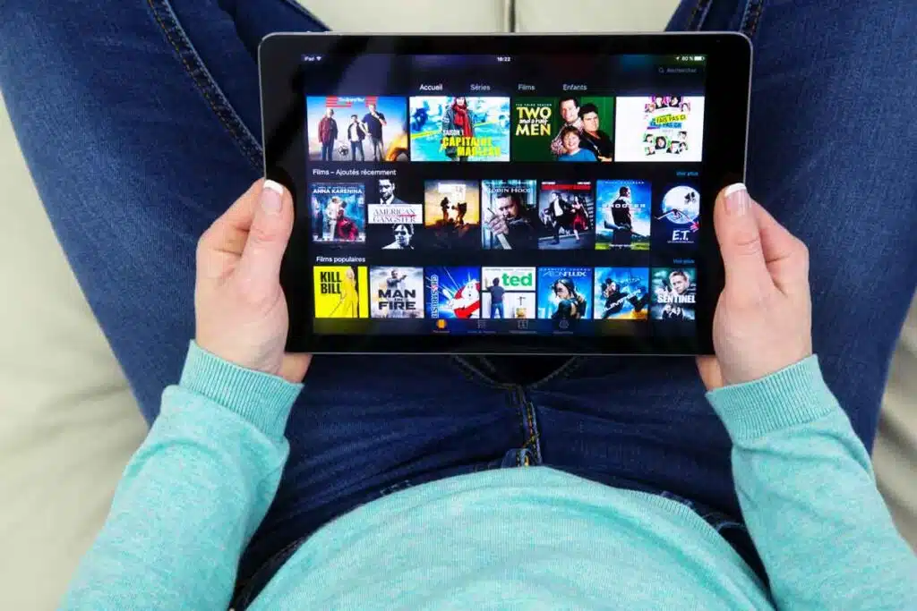 Close up of a woman holding a tablet with a streaming app displayed, representing the Gaia settlement.