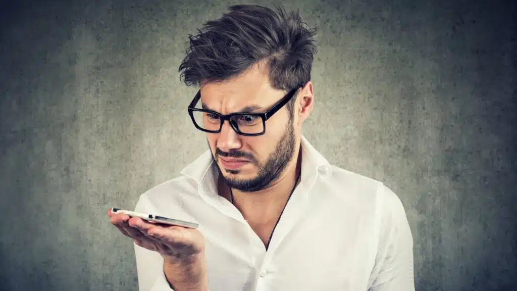 Young bearded man in shirt holding smartphone being upset with AI call.