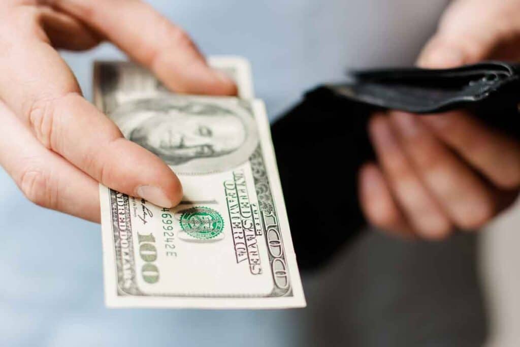 Close up of hand holding cash and a wallet, representing recent class action rebates.
