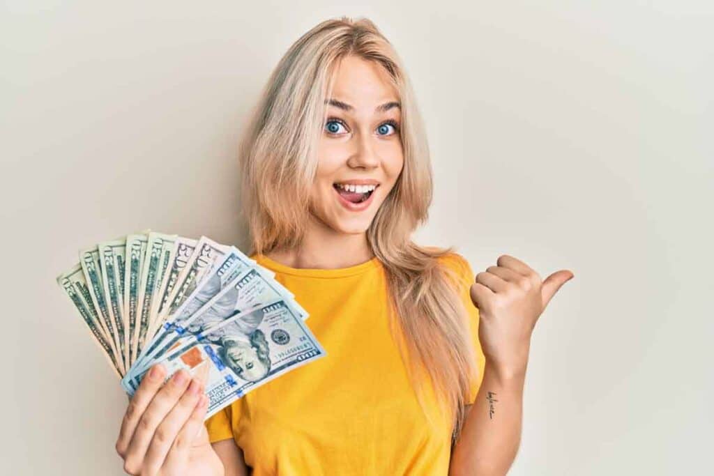 An excited woman holding US cash, representing checks in the mail.