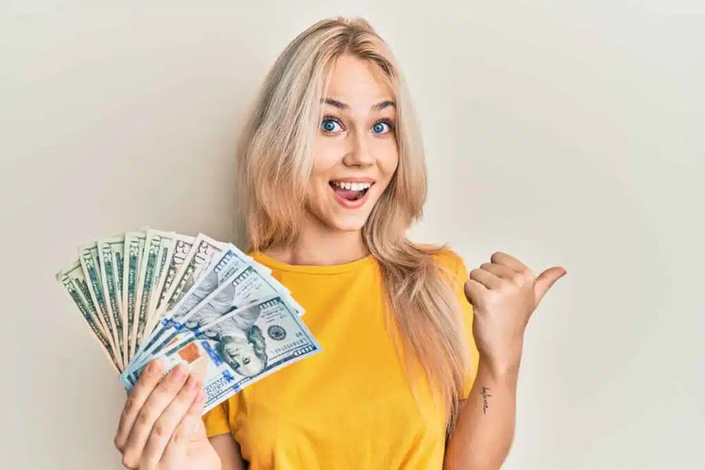 An excited woman holding US cash, representing checks in the mail.