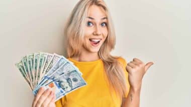 An excited woman holding US cash, representing checks in the mail.