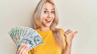 An excited woman holding US cash, representing checks in the mail.