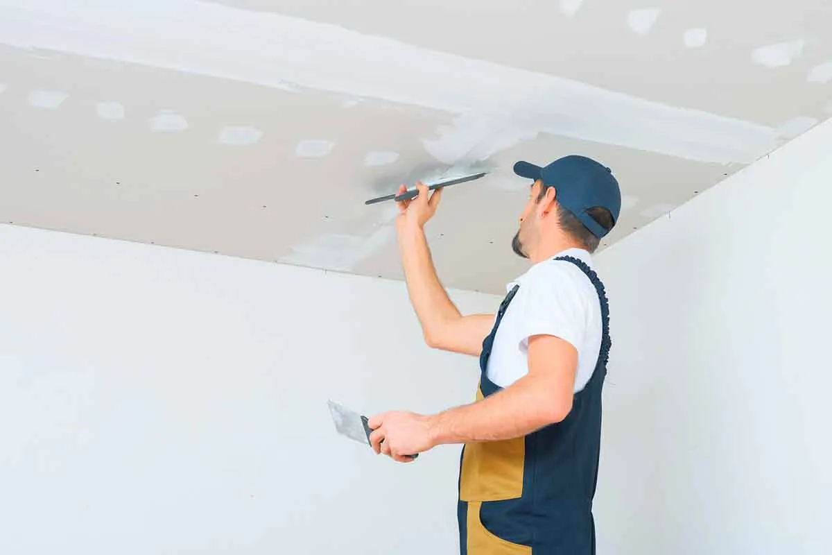 A drywall worker applying plaster to ceiling, representing the TBJ Drywall & Taping settlement.