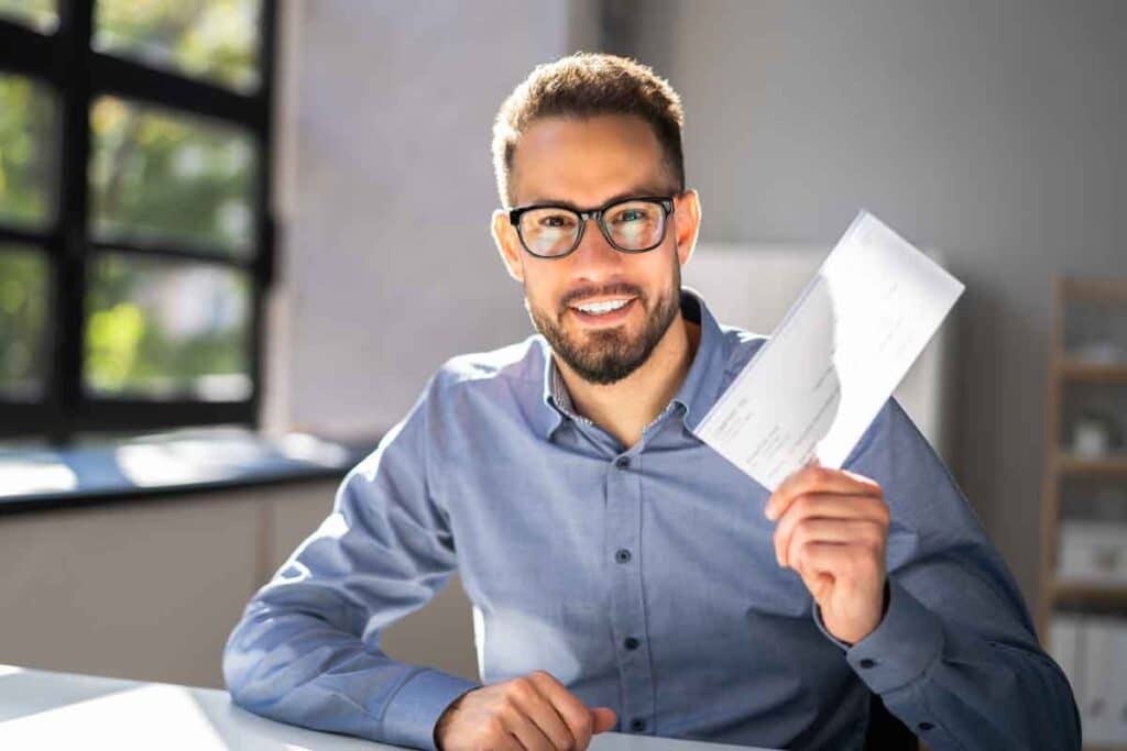 A happy man holding a check, representing checks in the mail.