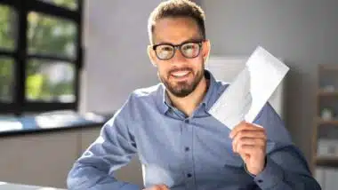 A happy man holding a check, representing checks in the mail.