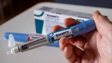 Hand holding Ozempic injection pen, representing weight loss drug risks.