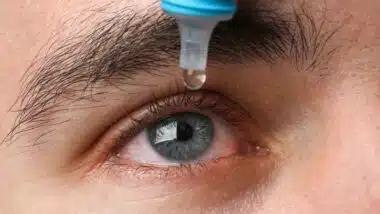 Close up of a man putting eyedrops in his eyes, representing the eye drop settlement.