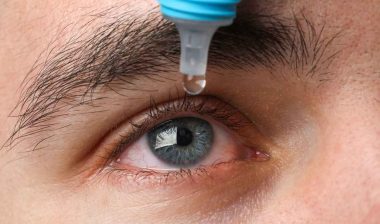 Close up of a man putting eyedrops in his eyes, representing the eye drop settlement.