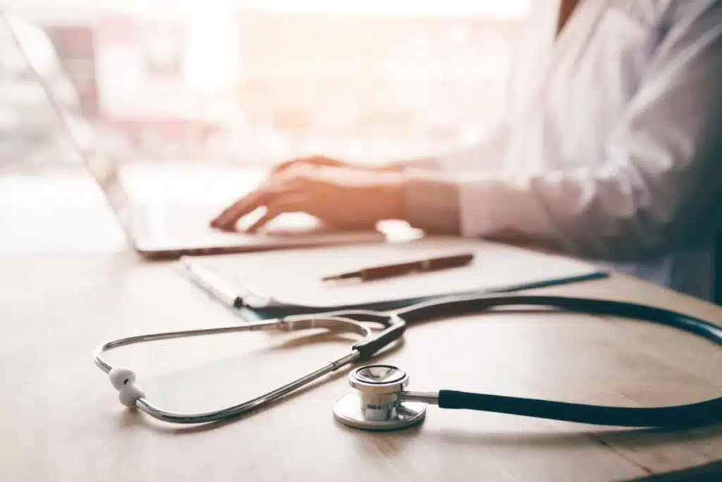 Close up of stethoscope next to a medical worker typing on a laptop, representing the Somnia settlement.
