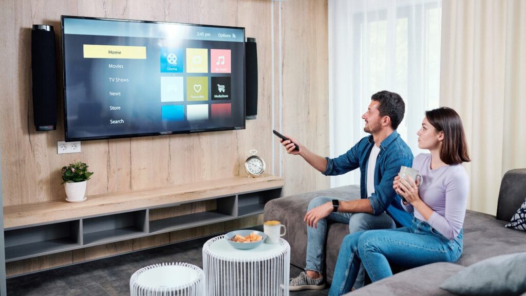 Young couple having tea while going to watch something on plasma tv panel