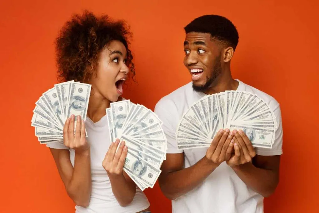 An excited couple holding U.S. cash, representing checks in the mail.
