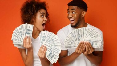 An excited couple holding U.S. cash, representing checks in the mail.