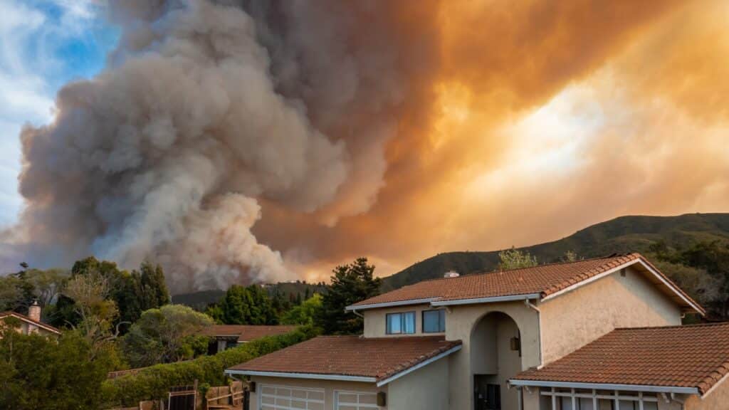 fire fills the sky with dark smoke and flames as it burns close to houses.