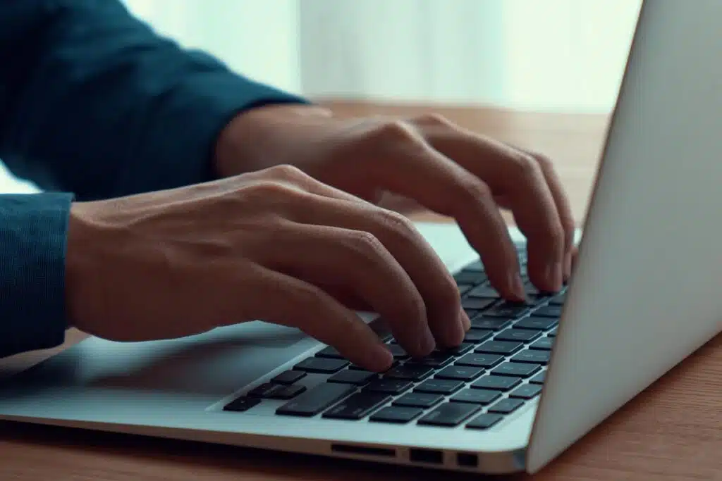 Close up of a mans hands typing on a laptop, representing the Crossbreed Holsters settlement.