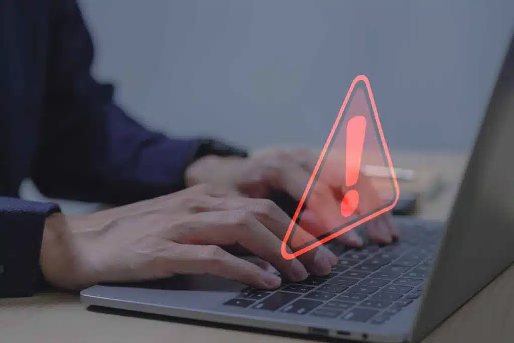 Close up of hands typing. on a laptop with a warning symbol overlay, representing the Marshall & Melhorn settlement.
