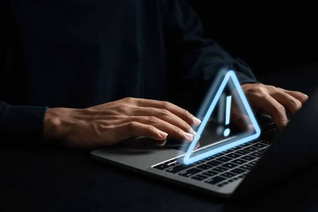 Close up of hands typing on a laptop with a warning symbol overlay, representing the Loren D. Stark Co. settlement.