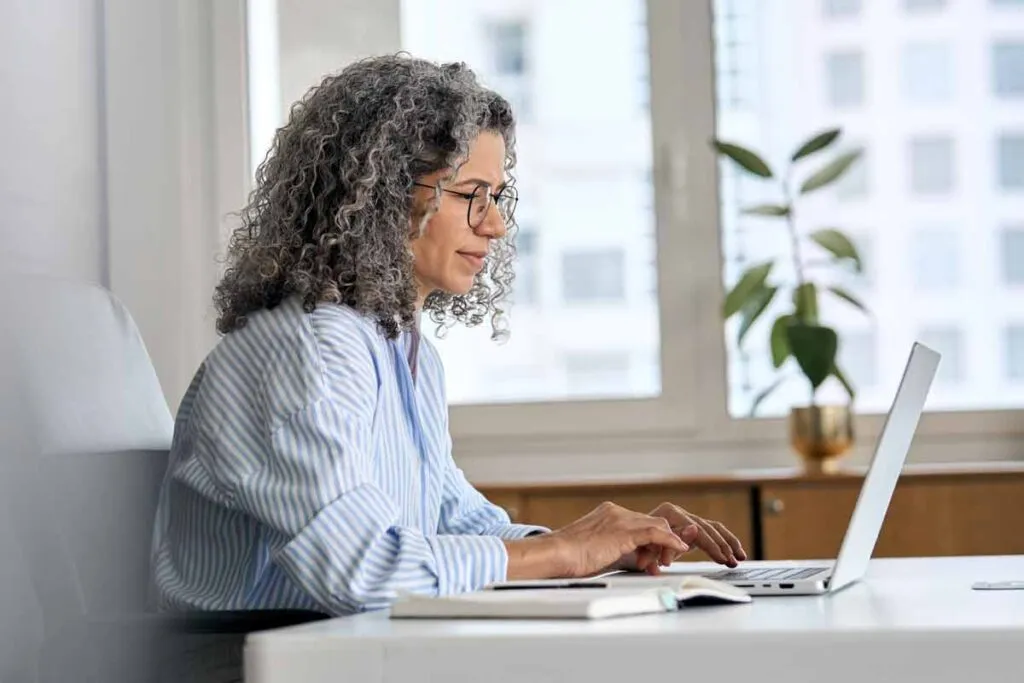 A woman using her laptop in a home office, representing the Luxottica settlement.