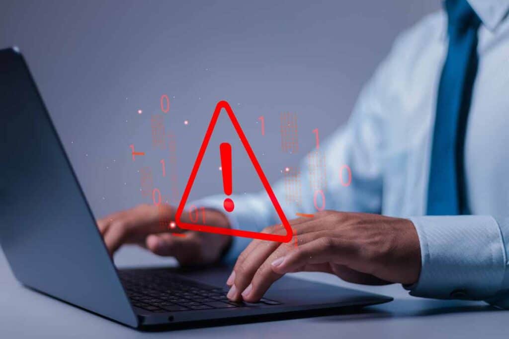 Close up of a worker typing on a laptop with a warning symbol overlay, representing the Builders Mutual settlement.