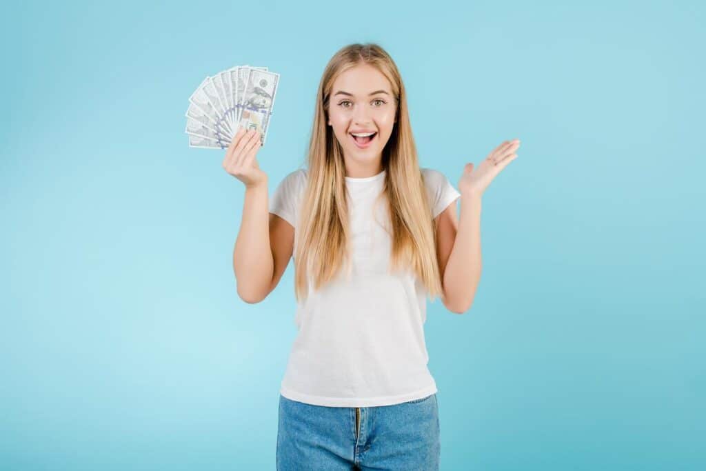 An excited woman holding U.S. cash, representing class action rebates for January 2025.