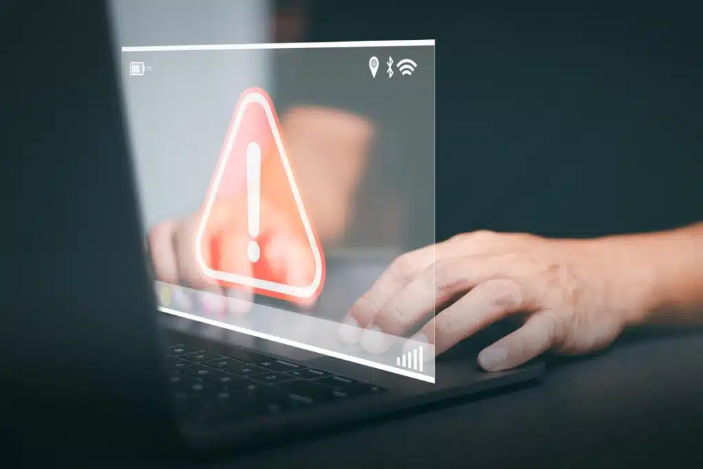 Close up of hands typing on a laptop with a warning symbol overlay, representing the Drug Free Workplaces settlement.