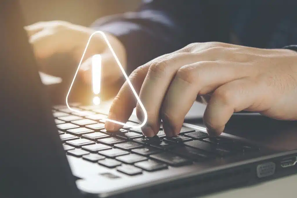Close up of hands typing on a laptop with a warning symbol overlay, representing the PowerSchool data breach.