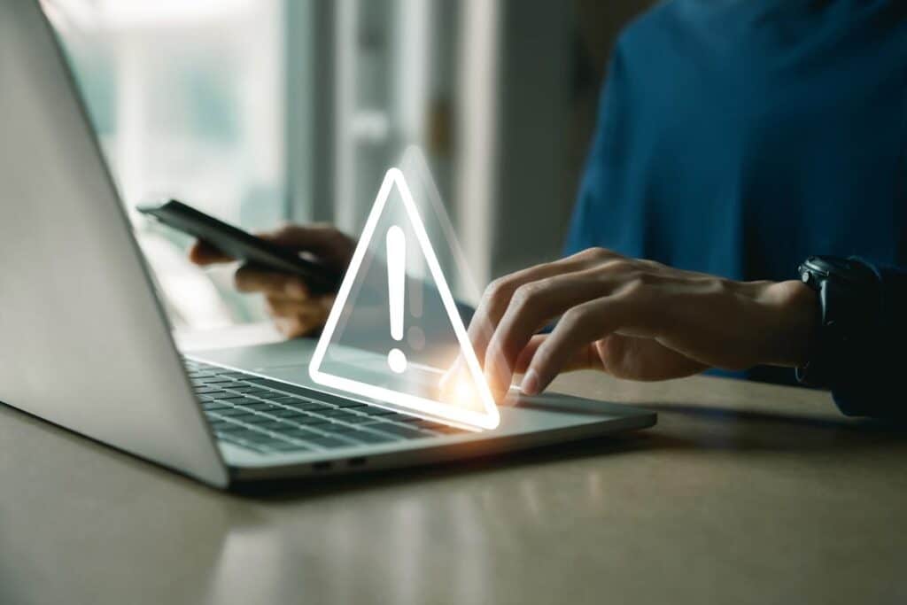 Close up of hands typing on a laptop with a warning symbol overlay, representing the Professional Finance Co. settlement.