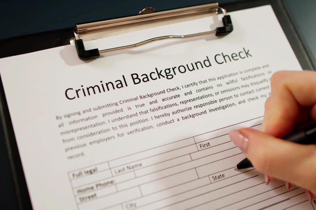 Close up of a hand filling out a criminal background check document, representing the Chestnut Hill Hospital settlement.