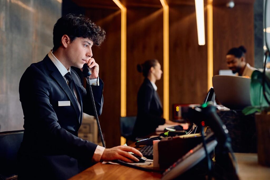 A hotel receptionist on the phone while using a computer, representing the hotel hack.