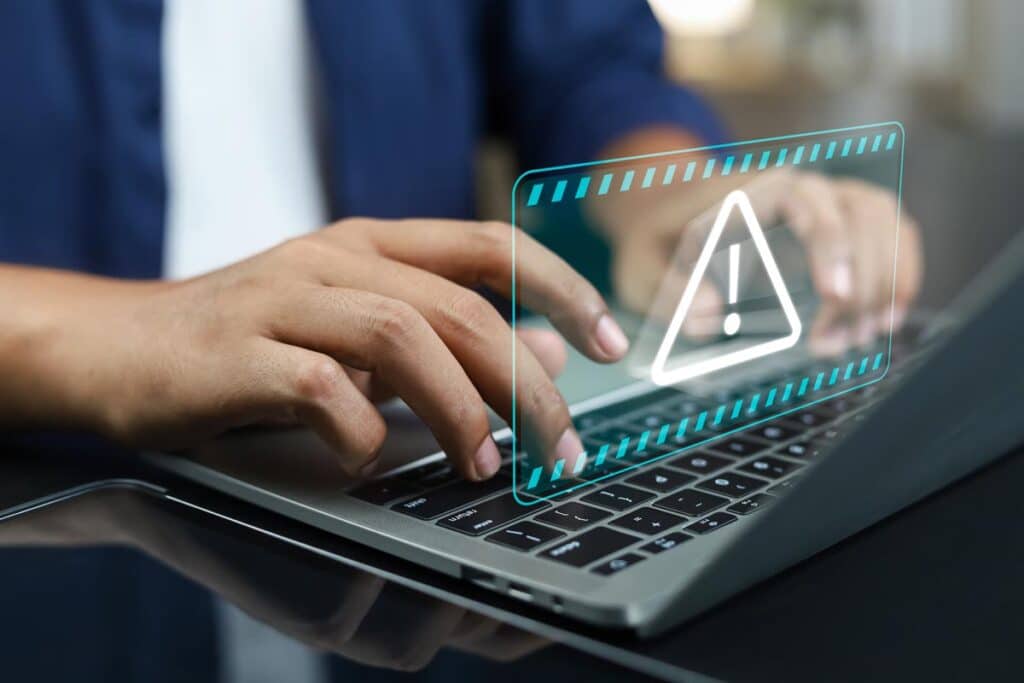 Close up of hands typing on a laptop with a warning symbol overlay, representing the RIBridges data breach.