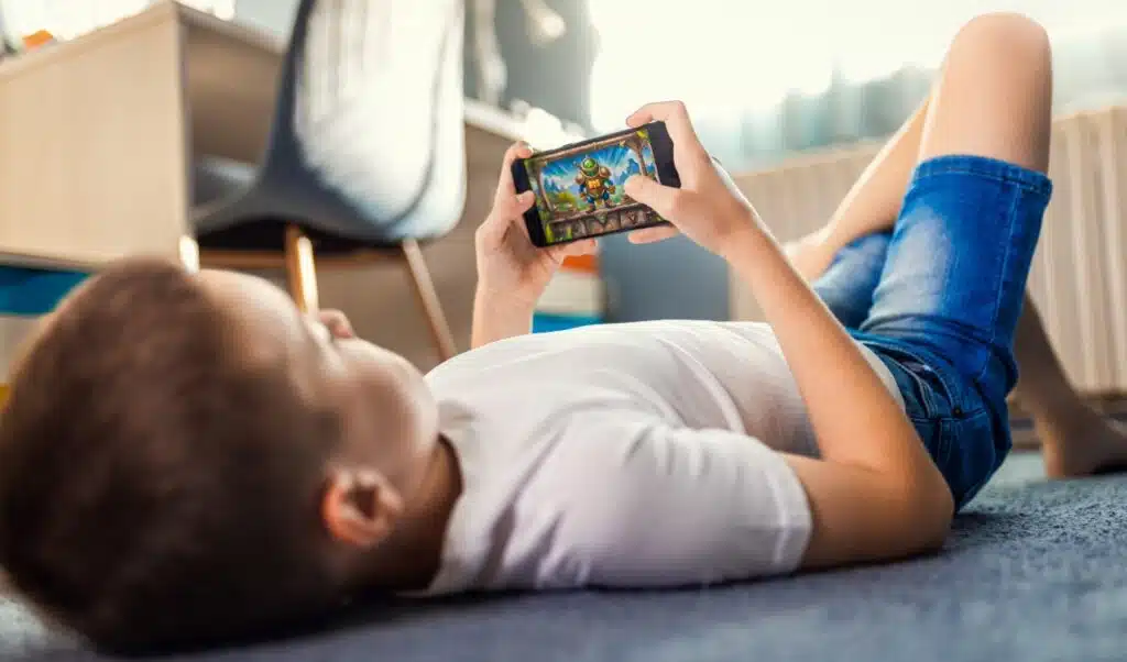 Boy playing video game on smartphone laying on floor in his room.