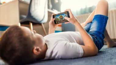 Boy playing video game on smartphone laying on floor in his room.