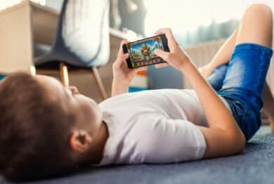Boy playing video game on smartphone laying on floor in his room.