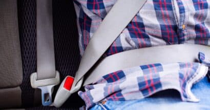 Photo of man in plaid shirt sitting in a car putting on seat belt.