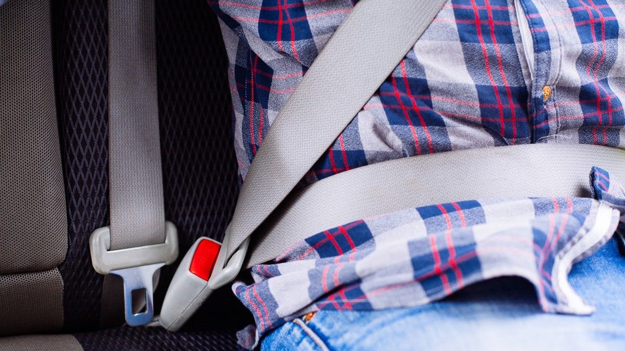 Photo of man in plaid shirt sitting in a car putting on seat belt.