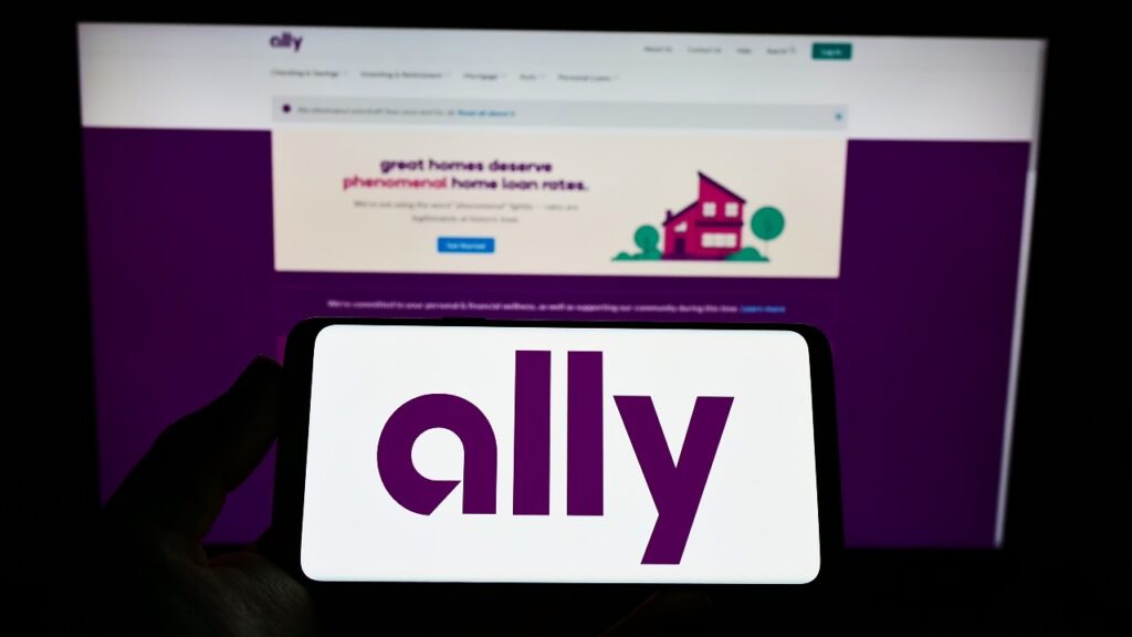 Person holding smartphone with logo of US financial services company Ally Financial Inc. on screen in front of website.